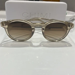 Beige runda solglasögon från Chimi - Snygga solglasögon från Chimi med transparent beige båge och runda linser i brun toning. Klassisk och trendig modell som passar perfekt till sommaren. Bågarna är i plast och har en stilren design med diskreta detaljer.