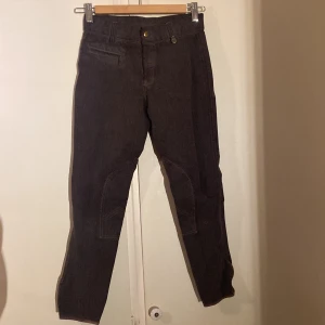 Mörkbruna ridbyxor från CRW, stl 150 - Snygga mörkbruna ridbyxor från CRW med förstärkta knäpartier och smart kardborre vid benslut. Byxorna har en klassisk passform och är perfekta för ridning. Tillverkade i slitstarkt bomullsmaterial med detaljer i brunt. Använda sparsamt och inga defekter. 