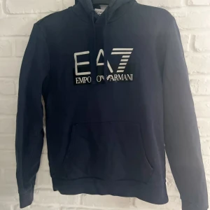 Mörkblå EA7 Emporio Armani hoodie - Snygg mörkblå hoodie från EA7 Emporio Armani med stor vit logga framtill står ingen storlek på men den bär storlek 168-175 så de är storlek S 