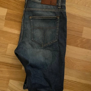Mörkblå jeans från tiger of sweden - Snygga mörkblå jeans från tiger of sweden med klassisk femficksdesign och slitningar framtill. Jeansen har raka ben och kontrastsömmar, samt en brun läderpatch med T/J-logga bak i midjan. Perfekta för en avslappnad och cool look.