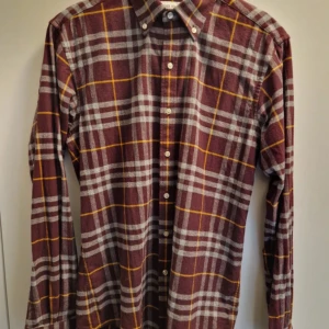 Rutig skjorta från John Henric - Snygg rutig skjorta från John Henric i vinrött med gråa och gula rutor. Skjortan har klassisk krage, knäppning framtill och långa ärmar. Perfekt för dig som gillar en stilren men ändå färgstark look.