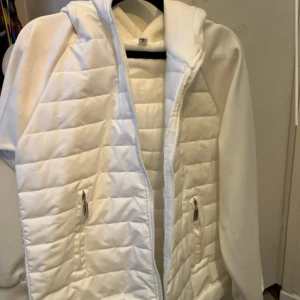 Vit quiltad cardigan. - Snygg vit puffer cardigan med quiltat mönster och dragkedja framtill. Jackan har huva, långa ärmar i mjukt material och två fickor med dragkedja. Perfekt för dig som vill ha en stilren och clean look. Passar som S och XS, ny pris 1300kr helt ny utan prislapp bara.