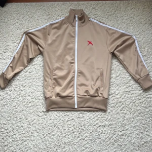 Beige track jacket från Axel Arigato - Beige track jacket från Axel Arigato. Den är i mycket bra skick, säljes då jag inte använder den. Vid behov av fler bilder eller info så är det bara att säga till. Tröjan är i storlek M.