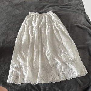 Vit långkjol i broderad bomull - Superfin vit långkjol i bomull med broderade blommor och hålmönster. Köpt i Korea. Kjolen har resår i midjan och ett romantiskt, luftigt fall. Perfekt för dig som gillar en feminin och somrig stil.