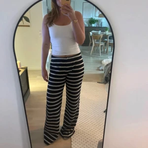 Svartvita vida byxor med mönster - Säljer ett par snygga svartvita byxor med vågigt randigt mönster. Byxorna har en vid passform och hög midja, perfekta för en chill och trendig look. Materialet känns mjukt och stretchigt, vilket gör dem riktigt bekväma att bära hela dagen.