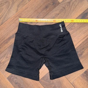 Svarta träningsshorts från DFYNE - Säljer ett par svarta träningsshorts från DFYNE med hög midja och tight passform. Shortsen är tillverkade i stretchigt syntetmaterial och har en scrunch-detalj bak för extra shaping. Perfekta för gymmet eller andra sportaktiviteter. Otroligt sköna och definierar kroppen! 