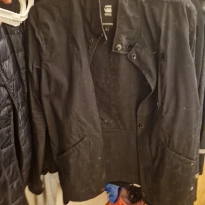 Svart jacka från G-Star Raw, storlek L - Svart jacka från G-Star Raw med snygga knappar framtill och två stora fickor. Jackan har en stilren design och är tillverkad i ett slitstarkt material. Perfekt för dig som gillar streetwear och vill ha en klassisk look.pris kan diskuteras vid snabbaffär o jag kan mötas i sthlm jag kommer såklart håra av den o tvätta den om du ska köpa