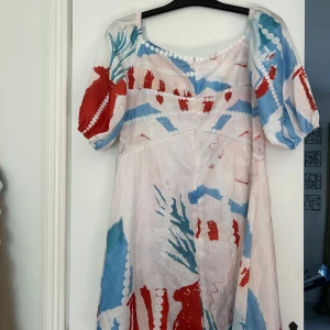 Färgglad kortklänning med puffärm - Säljer en unik kortklänning med puffärmar och fyrkantig urringning. Klänningen har ett färgstarkt mönster i rött, blått och vitt med abstrakta former och prickar. Tillverkad i lätt bomull, perfekt för sommarens alla tillfällen. Snygg och bekväm passform.