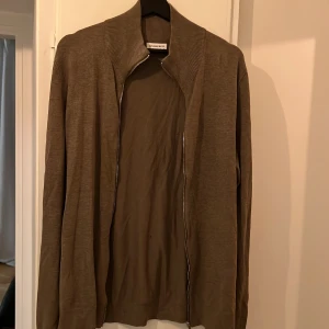 Beige kofta med dragkedja från Lindbergh - Säljer en beige kofta från Lindbergh med dragkedja framtill och ribbad krage. Koftan har lång ärm och är tillverkad i ett mjukt material som känns skönt mot huden. Perfekt för lager-på-lager och enkel att matcha med olika outfits.