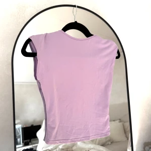 Ljuslila crop top med öppen rygg!  - Säljer en ljuslila croppad topp med öppen rygg i storlek XS. Toppen är ärmlös med breda axelband och har en snygg öppen ryggdetalj. Tillverkad i mjukt och stretchigt syntetmaterial.