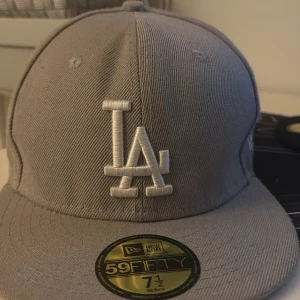 Grå LA Dodgers keps från New Era - Säljer en grå 59FIFTY keps från New Era med LA Dodgers broderat i vitt framtill och 1988 World Series broderat på sidan. Har använt i ett halvår och nu behöver jag inte den så jag säljer