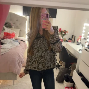 Leopardmönstrad blus med volang - Säljer en snygg blus med leopardmönster och svarta volangdetaljer. Blusen har långa ärmar och en lös passform, från Lindex storlek 158/164