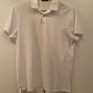 Vit piké från Massimo Dutti - Klassisk vit pikétröja från Massimo Dutti med krage och knapp framtill. T-shirten är kortärmad och tillverkad i mjuk bomull, perfekt för en clean och stilren look. Passar dig som gillar enkel och tidlös stil.