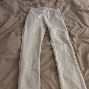 Ljusgrå mjukisbyxor från Gina Tricot - Superbekväma ljusgrå mjukisbyxor från Gina Tricot med snörning i midjan och två bakfickor med broderad detalj. Byxorna har normal passform och är perfekta för chill dagar. Tillverkade i mjukt bomullsmaterial. Storlek L i 14+ på Gina tricot, skulle säga M vuxen storlek 