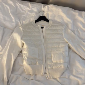 Vit quiltad jacka från Gina Tricot - Snygg vit jacka från Gina Tricot med quiltad framsida och två fickor. Jackan har ribbade muddar, långärmade stickade ärmar och dragkedja framtill. Perfekt för dig som gillar stilren och fräsch look.