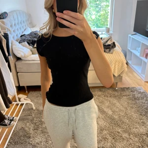 Svart ribbad topp med kort ärm - En svart, tight ribbad topp med rund halsringning och korta ärmar. Enkel och stilren modell som sitter figurnära och är perfekt att matcha med jeans eller kjol. Mjuk och stretchig känsla.