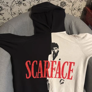 Scarface hoodie  - Säljer en riktigt snygg hoodie med Scarface-tryck. Tröjan är delad i svart och vitt med stor röd Scarface-text och ikoniskt motiv framtill. Säljer då tröjan blivit liten för mig. 44 cm i midjan och 14 cm axel. 
