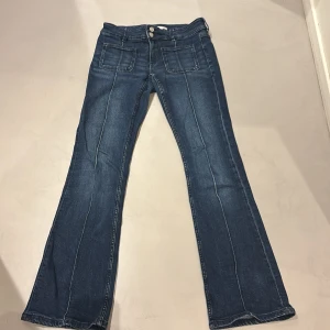 Blå bootcut jeans från Gina Tricot - Snygga blå low waist jeans från Gina Tricot i bootcut-modell med markerade sömmar framtill och stora fickor. Jeansen har dubbla knappar i midjan och är tillverkade i klassiskt denimtyg. Perfekta för dig som gillar en retroinspirerad look. 