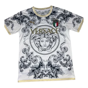 Versace-Puma-Italien  - Unik vit högkvalitativ fotbollströja från Puma med Versace-design och Italiens emblem. Tröjan har korta ärmar, guldiga detaljer och ett stort Medusa-motiv i svart och grått. Tillverkad i lätt och ventilerande material, perfekt för dig som vill sticka ut på planen.