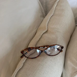 Bruna ovala glasögon med sköldpaddsmönster - Säljer ett par snygga glasögon med oval form och klassiskt sköldpaddsmönster i bruna och svarta toner. Bågarna är i plast och har en tidlös vibe som passar till många olika stilar. Perfekta om du vill ha en cool och trendig look.