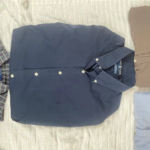 Mörkblå skjorta från Ralph Lauren - Snygg mörkblå skjorta från Ralph Lauren med klassisk krage och vita knappar. Skjortan är gjord i mjuk bomull med lite stretch för extra komfort. Perfekt för dig som gillar stilrena plagg med diskret broderad logga på bröstet. Skjortan har en liten fläck på sig (se sista bild), det är ända defekten🙌