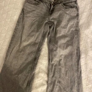 Grå jeans med raka ben - Säljer ett par grå jeans med raka ben och klassisk femficksdesign. Jeansen har snygga detaljer på bakfickorna med lock och knapp, samt en cool tvättad look. Perfekta för dig som gillar en avslappnad och stilren vibe. Gina tricot ”low rise baggy” storlek 164🤗 