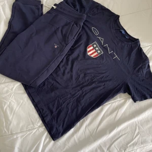 Mörkblå GANT t-shirt med mjukis byxor - Snygg mörkblå t-shirt och mjukis byxor från GANT med stort tryck av logga och sköld på bröstet. Klassisk rund halsringning och korta ärmar. Tillverkad i mjuk bomull som känns skön mot huden. Perfekt för dig som gillar stilrena och sportiga plagg. Köpt på Hede Fashion. Passar mig som är en liten S / XS