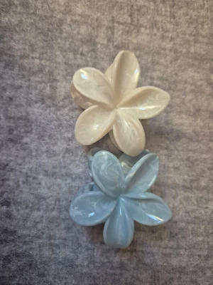 2 hårklämmor i ljusblå och vit - Bilderna visar två hårklämmor formade som blommor i pärlemorvit och ljusblå färg.