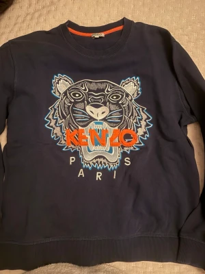 Äkta Mörkblå Kenzo sweatshirt med tiger - Säljer en mörkblå sweatshirt från Kenzo i storlek L  men den är som S, med ikonisk broderad tiger och logga i orange, blått och vitt på bröstet. 