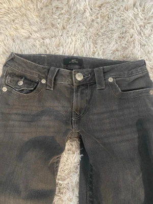 True Religion Joey Low Rise Flare Jeans - Säljer ett par svarta True Religion Joey Low Rise Flare jeans i storlek 25. De har låg midja, utsvängda ben. Klassisk True Religion-logga baktill. Nypris 1300kr, säljer då de inte passar mig. Aldrig använda 🫶