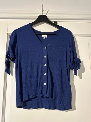 Marinblå blus från Bubbleroom  - Marinblå blus i storlek S från Bubbleroom. Knappar framtill och knytdetalj i ärm. Blusen är gjord i viskos.
