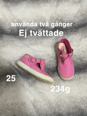 Rosa tygskor från Cienta, storlek 25 - Säljer ett par rosa tygskor från Cienta med rund tå och vit platt sula. Skorna har ett spänne över foten. Perfekta för dig som gillar färgglada och bekväma skor till vardags🌸 .Använda två gånger. Ej tvättade. Storlek 25