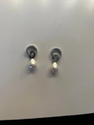 Örhängen  - Bilden visar ett par örhängen med pärldetaljer, ingen väst finns med.