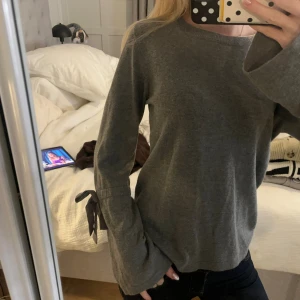 Grå tröja med knyt från Holly & Whyte - Säljer en grå långärmad tröja från Holly & Whyte by Lindex i storlek S. Tröjan har snygga knytband vid ärmsluten som ger en extra detalj. Mjuk och skön, perfekt för dig som gillar enkel stil med twist.