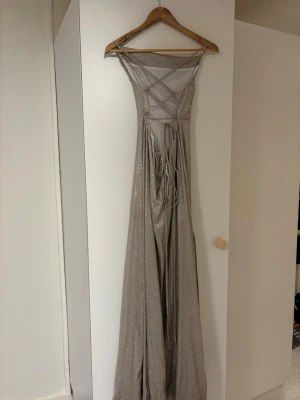 Glittrig långklänning från JJ's House - Säljer en glittrig långklänning från JJ's House i storlek S. Klänningen är champagnefärgad med smala axelband, snörning i ryggen. Materialet har en skimrande finish som ger extra lyxig känsla. Perfekt för speciella tillfällen! Använd endast 1 gång!