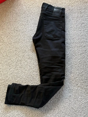 Replay Anbass svarta slim jeans - Svarta Replay Anbass Hyperflex jeans i slim fit med klassisk femficksdesign och bälteshällor. Materialet är stretchigt, perfekt för dig som gillar en smal siluett. Snyggt Replay-märke på bakfickan och diskret logga vid linningen. Sitter ganska tight.