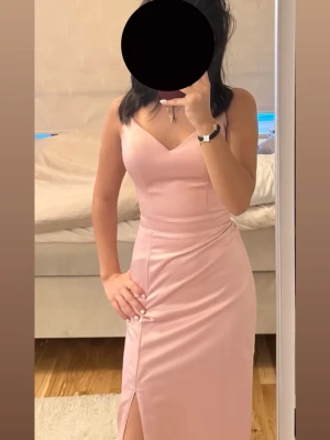 Ljusrosa långklänning från L&S - Supersnygg ljusrosa långklänning från Seres med smala axelband, v-ringning och en stilren slits framtill. Klänningen har en figurnära passform och är gjord i ett glansigt, mjukt material som känns lyxigt. Perfekt för dig som vill sticka ut med en elegant look.
