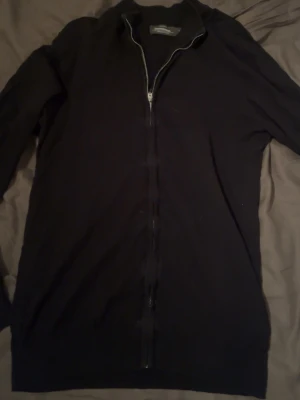 Svart kofta med dragkedja Dressmann storlek S - Svart kofta från Dressmann i Supima bomull, storlek S. Koftan har hel dragkedja framtill och ribbad krage. Perfekt för dig som gillar stilrena och enkla plagg med snygg passform. Passar till många olika outfits och är riktigt skön att ha på sig.
