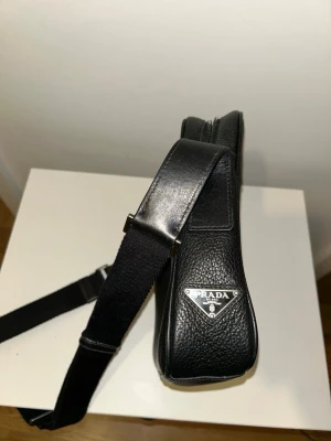 Prada Axelväska i Kalvskinn - Supersnygg Prada väska i läder. En elegant och mångsidig accessoar med justerbar axelrem och snygga detaljer. Passar till alla tillfällen.