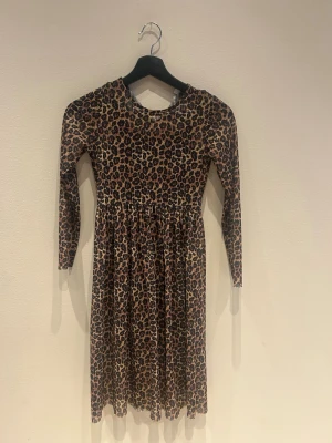 Leopardmönstrad långärmad klänning Name It - Säljer en långärmad klänning från Name It i storlek 134. Klänningen har ett snyggt leopardmönster i bruna och svarta toner, rund hals och ett lätt rynkat midjeparti som ger en fin siluett. Perfekt för dig som gillar djurmönster och vill sticka ut.