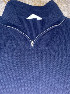 Mörkblå stickad half zip tröja - Säljer en mörkblå stickad tröja med half zip och hög krage. Tröjan har långärmade och är ribbstickad för extra struktur. Perfekt för dig som gillar en enkel men snygg look med lite sportig touch.