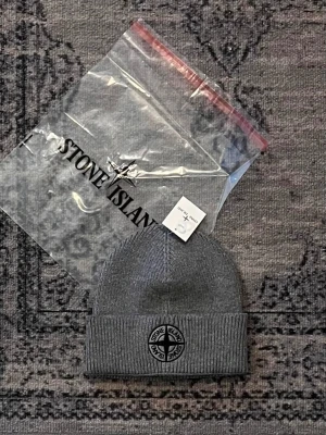 Stone Island mössa - Säljer en grå mössa från Stone Island med klassisk logotyp framtill. Mössan är ribbstickad och har uppvikt kant för extra komfort. Perfekt för att hålla värmen och samtidigt se snygg ut. MED PRISLAPP, HELT NY! Jag finns även på vinted (kevorkkihiayan). Mössan passar både mån och kvinnor. 