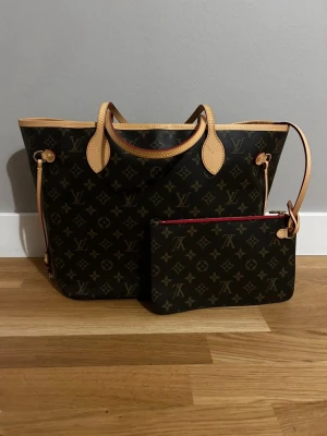 Louis Vuitton Monogram Shoppingväska - Priset kan diskuteras vid snabb affär. Säljer en klassisk Louis Vuitton Neverfull shoppingväska i brunt monogrammönster med beige detaljer och röda inslag. Väskan är tillverkad i läder och har en matchande clutch med dragkedja som kan fästas på väskan. Insidan är röd. Postas omgående. Bara att skriva för ännu mer bilder på detaljer mm. Inga skavanker alls.