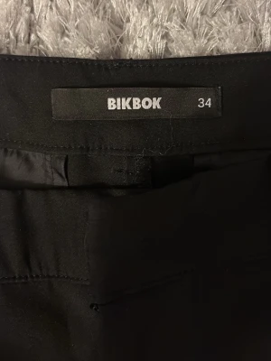 Svarta kostymbyxor från Bik Bok - Snygga svarta kostymbyxor från Bik Bok i storlek 34. Byxorna har klassisk rak passform med bälteshällor och sidofickor. Perfekta att styla med en cool topp eller hoodie. Materialet känns mjukt och har en lätt stretch för extra komfort.