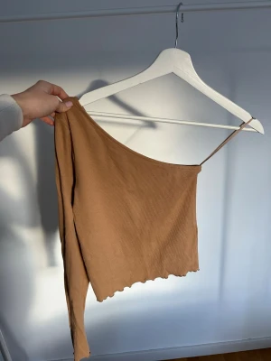 Beige ribbad oneshoulder topp - Kamelfärgad one shoulder topp med lång ärm från Gina, fina detaljer i sömmarna, stl s