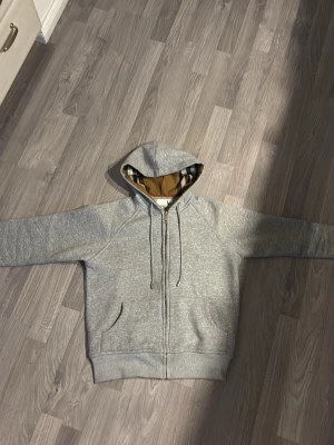 En Burberry tröja i storlek smal med grå färg och rutigt utseende i luvan  - Tröjan är i perfekt skick använt 0 gånger den e testad men passa inte mig så jag säljer den,tröjan är äkta och passar till alla outfits