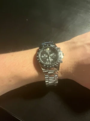 Hugo Boss Klocka  - Bilderna visar en klocka från Hugo Boss i silverfärgat rostfritt stål med svart urtavla och kronograf-detaljer, klockan har 10 ATM vilket betyder att den är vattentät till 10 meter. Klockan har plasten kvar då det är ett nytt armband från BOSS då det orginala hade mycket med skrapor, den har också ett nytt batteri och nästintill helt nytt glas. Nypris 1999 på ditur.se mitt pris 999, nytt armband för 349 och batteri för 250kr