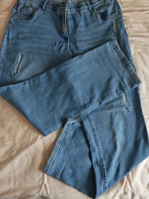 Jeans i str.46 Straight & Stretch från Ulla Popken - Säljer ett par ljusblå Mandy Straight jeans från Ulla Popken i storlek 46. Modellen har klassisk femficksdesign, raka ben och diskreta slitningar framtill. Jeansen är tillverkade i bomull och har en bekväm midja med knapp och dragkedja.ganska sköna och stretchiga. I bra skick. Inner mått 81 cm.