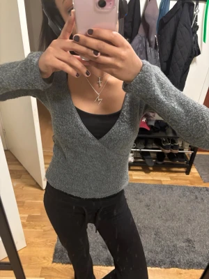 Grå omlottstickad tröja - Säljer en grå stickad tröja med omlott-design och v-ringad hals. Tröjan har lång ärm och är i en mjuk, lite fluffig stickad kvalitet. 