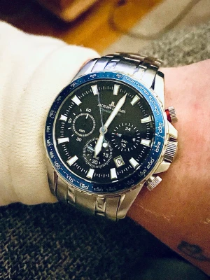Jacques Lemans Liverpool Klocka i nyskick!. - Den avbildade klockan är en Jacques Lemans Liverpool kronograf. Den specifika modellen matchar troligen referensnumret 1-2099E, som har en silverfärgad boett och länk i rostfritt stål med en svart urtavla och en blå infattning (bezel).  Specifikationer och detaljer Märke och serie: Jacques Lemans, Liverpool. Modellnummer: Troligen 1-2099E. Det finns liknande varianter som 1-2099A och 1-2099F. Såldes o säljs fortfarande för runt 1979kr - 2300kr online nu 